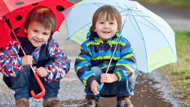 Two smiling children squatting under umbrellas